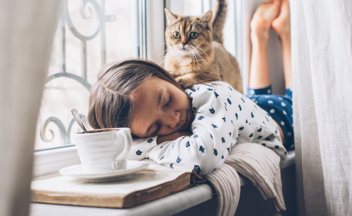 Jeune fille en pyjama couchée en train de dormir avec son chat assis sur son dos