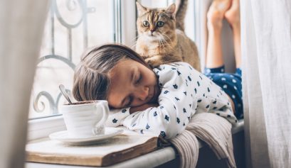 Jeune fille en pyjama couchée en train de dormir avec son chat assis sur son dos