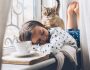 Jeune fille en pyjama couchée en train de dormir avec son chat assis sur son dos
