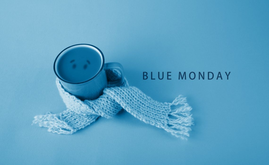 Un mug entouré d'une écharpe bleue avec écrit à côté : le Blue Monday, le jour le plus triste de l'année