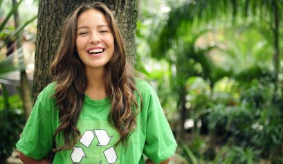 Adolescente qui sourit, posée contre un arbre et portant un t-shirt vert recyclage