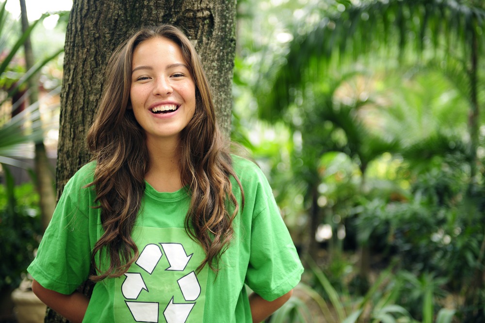 Adolescente qui sourit, posée contre un arbre et portant un t-shirt vert recyclage