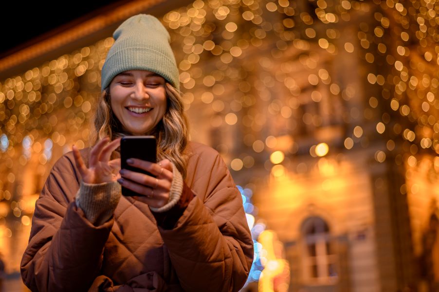 Une femme utilise son téléphone dehors avec des décorations de Noël en arrière plan