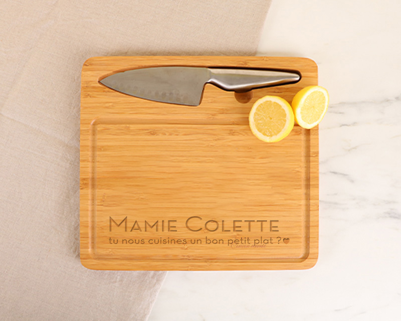 Cadeau Fête des grands-mères : planche à découper en bambou gravée 'Les petits plats de Grand-Mère' avec couteau intégré, sur plan de travail de cuisine.