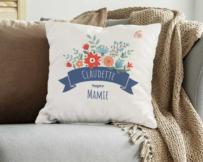 Cadeau personnalisé Fête des grands-mères 2025 : coussin 'Mamie fleurie' sur fauteuil en osier avec plantes environnantes.