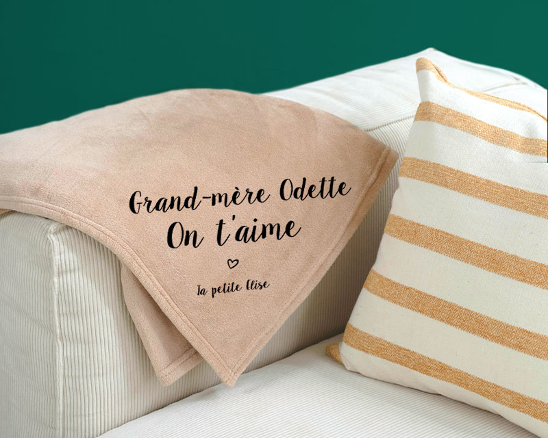 Cadeau Fête des grands-mères : maxi plaid en polaire écru personnalisé 'Mamie [Prénom], on t'aime' sur canapé beige.