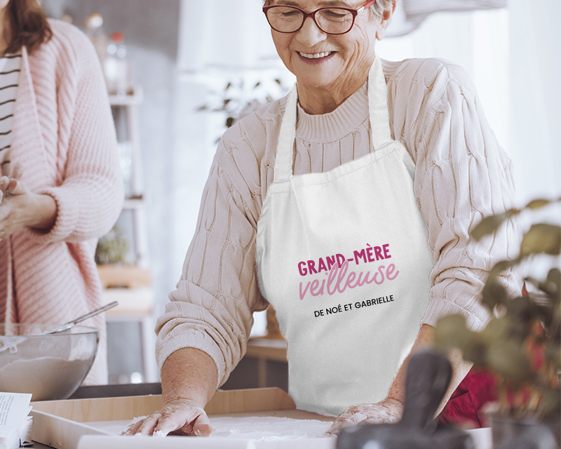 Cadeau Fête des grands-mères : tablier de cuisine blanc 'Grand Mère-veilleuse' avec message personnalisé, porté par une grand-mère souriante en cuisine.